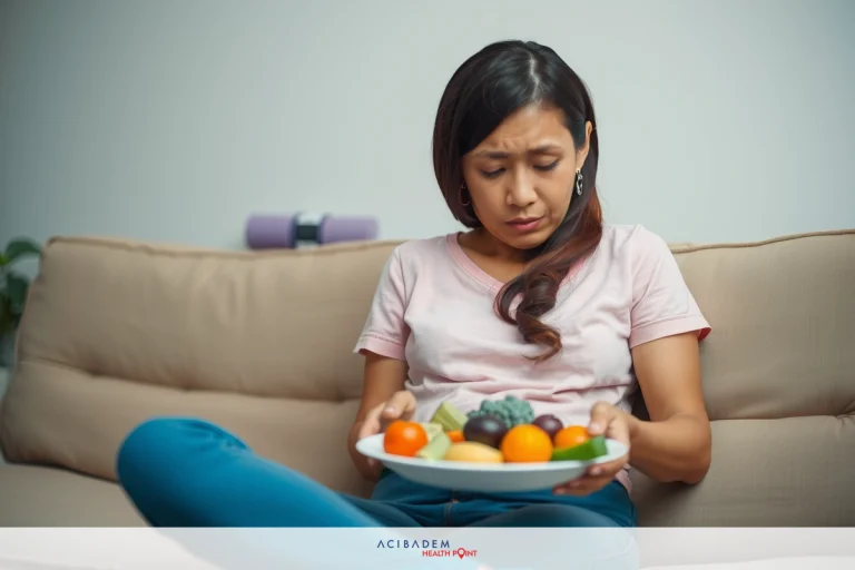 The image shows a woman sitting on a couch, holding a plate of fresh fruits and vegetables. Her expression appears to be one of concern or worry, suggesting she might not enjoy the taste or health benefits of consuming these foods.