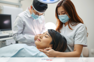 Medical professionals performing medical examination in a clinic setting. A patient is seated in a chair with headrest.